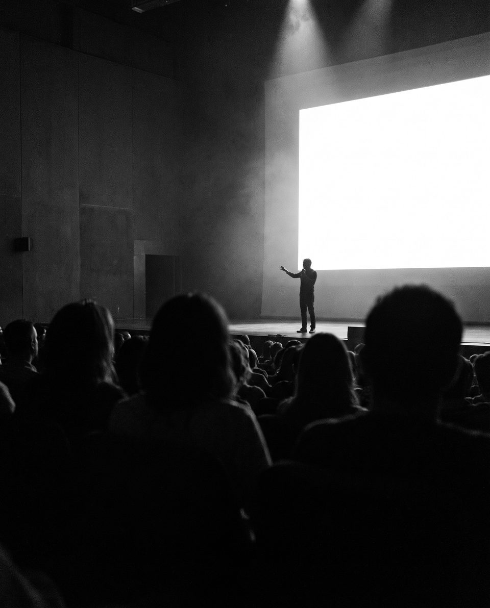 An audience in silhouette watching a presenter on stage